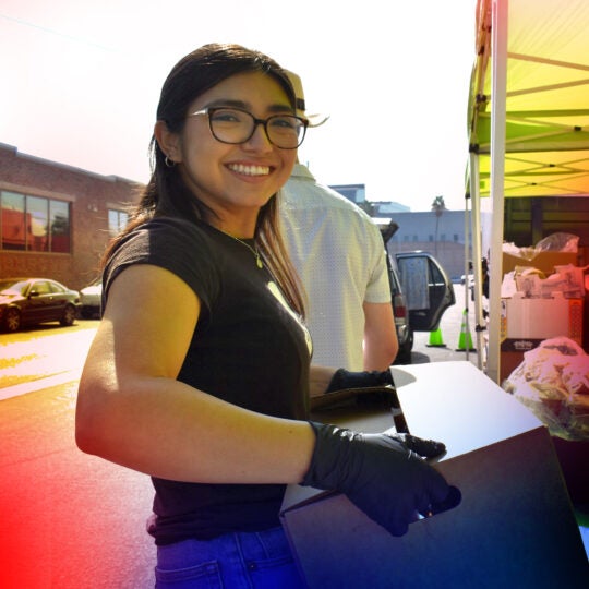 Student volunteering with food pantry, carrying box in her hands and looking at camera